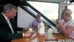 Reife blonde Haushaltshilfe und junge Blondine sitzen mit gut gekleidetem Mann am Kaffeetisch im hellen Wohnzimmer